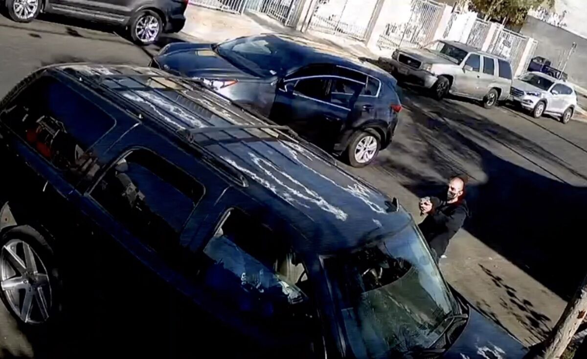 In an image from video, a man points a gun into a vehicle.