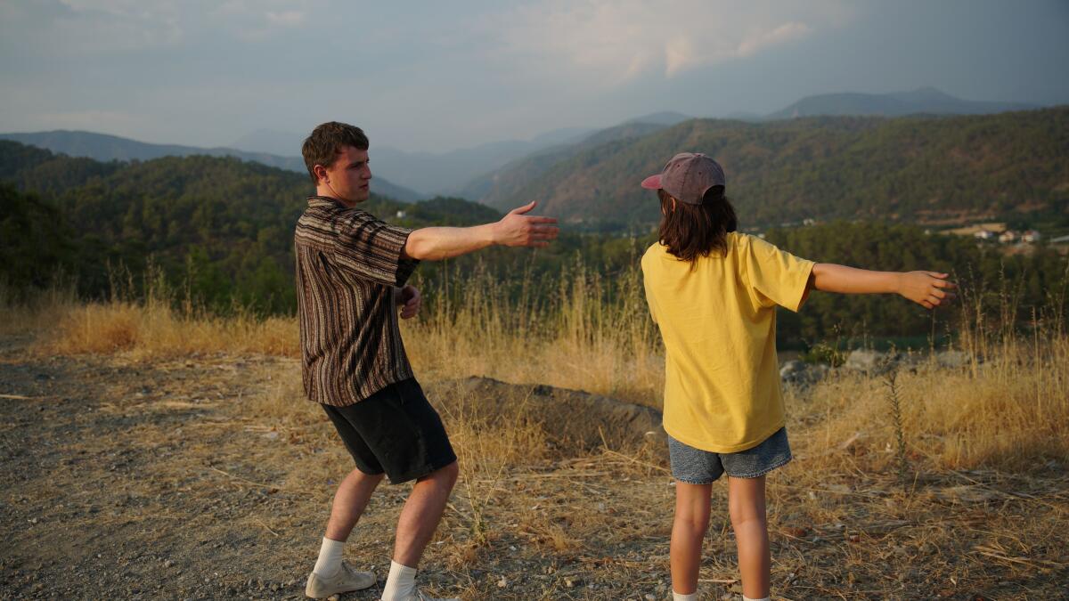 A man and a girl do a dance in a field with low mountains in the background  