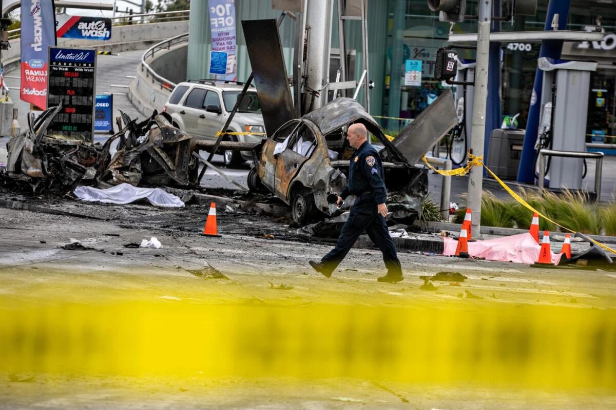 A man in dark blue uniform walks past wreckage of vehicles 