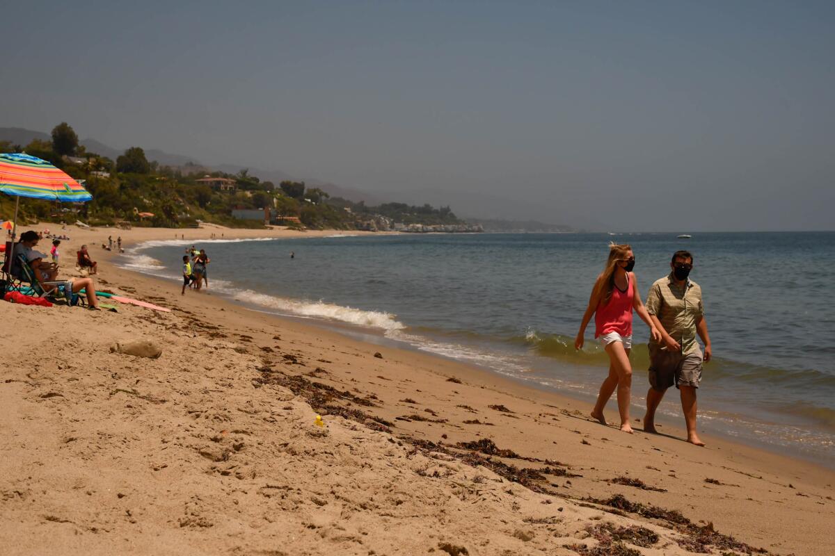 Beachgoers stroll in masks at Paradise Cove in Malibu.