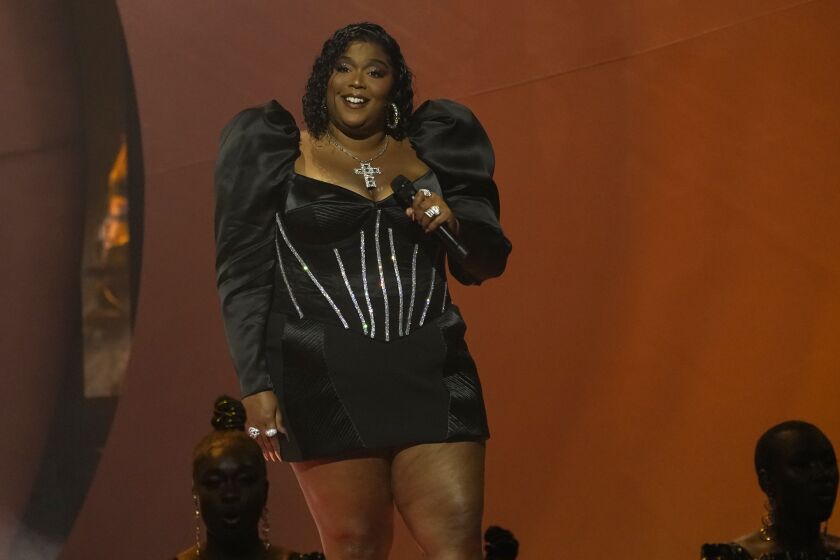 Lizzo wears a black dress and holds a microphone onstage