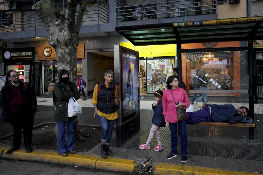 Los viajeros esperan un autobús mientras un hombre duerme en un banco, en Buenos Aires, Argentina, el viernes 12 de abril de 2024. (AP Foto/Natacha Pisarenko)