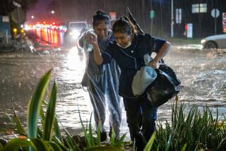 MONTECITO, CA - JAN. 9, 2022: Rosa Gallardo, left, and Connie Duarte cross a flooded street in Montecito after getting off work at their hotel job. (Michael Owen Baker / For The Times)