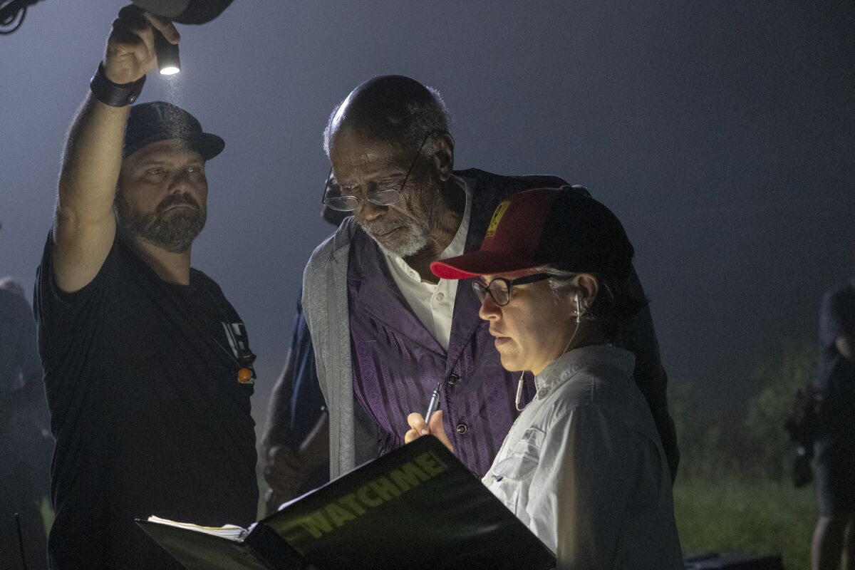 Louis Gossett Jr. and Nicole Kassell look at a binder she's holding with "WATCHMEN" on the cover while another man shines a flashlight.