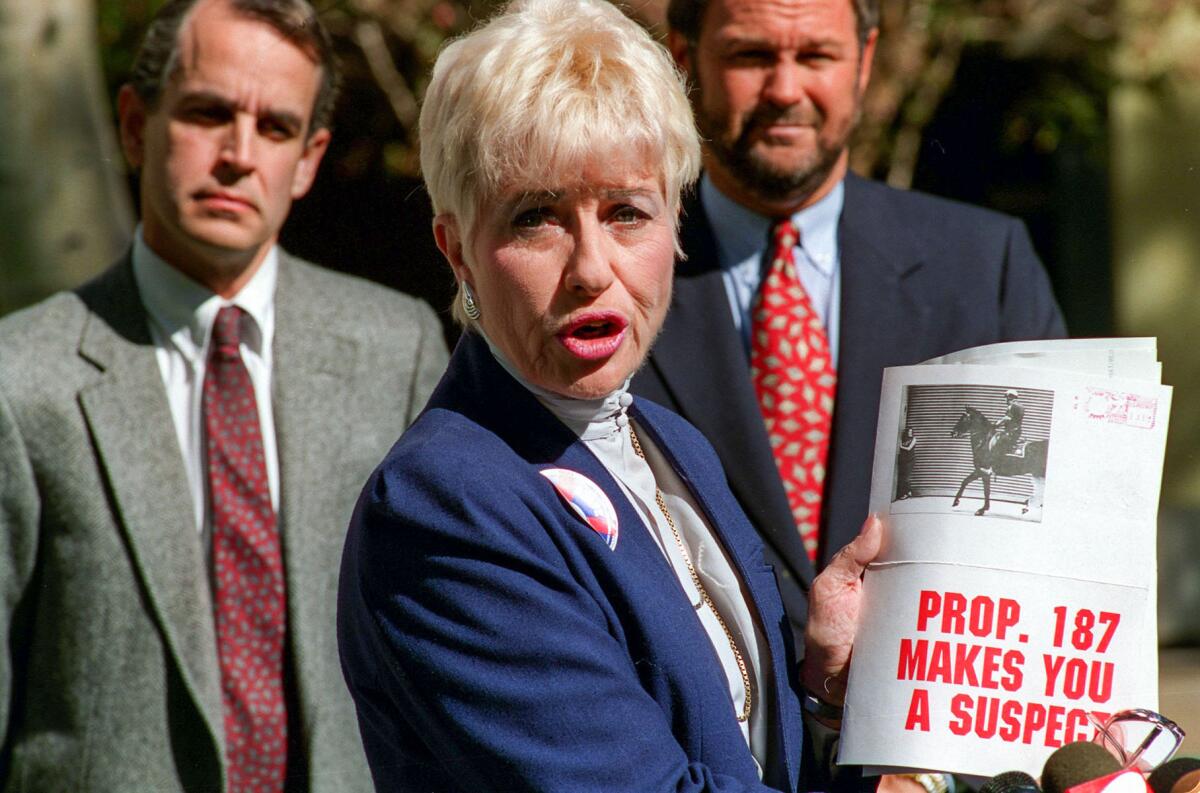 Nov. 4, 1994: Barbara Coe , spokesperson for Proposition 187, displays literature distributed by anti-Proposition 187 group at a news conference called to denounce what her organization sees as encouragement from the schools to students who walk out to protest the proposition. At rear is Ron Prince of Proposition 187 organization, left, and Rep. Dana Rohrabacher, a Proposition 187 supporter.