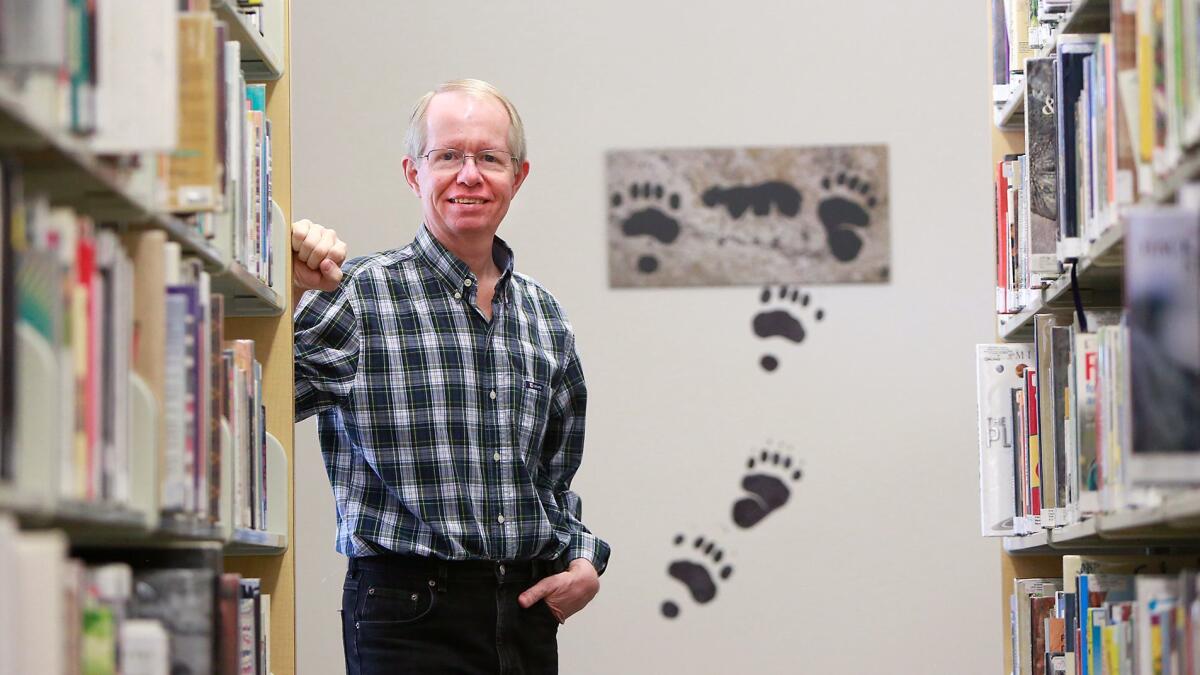 Robert Meyer stands with a sample of his prehistoric style of art of local animals and their tracks that he painted on the walls of the Library of the Canyons in Silverado Canyon.