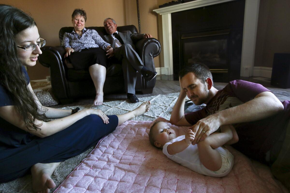 Brian Stoll plays with his 5-month-old daughter, Everly, as his wife, Rachael, looks on while her mother, Michelle Bacca-Llamas, and stepfather, Hector Llamas, laugh from the love seat at their home in West Jordan, Utah.