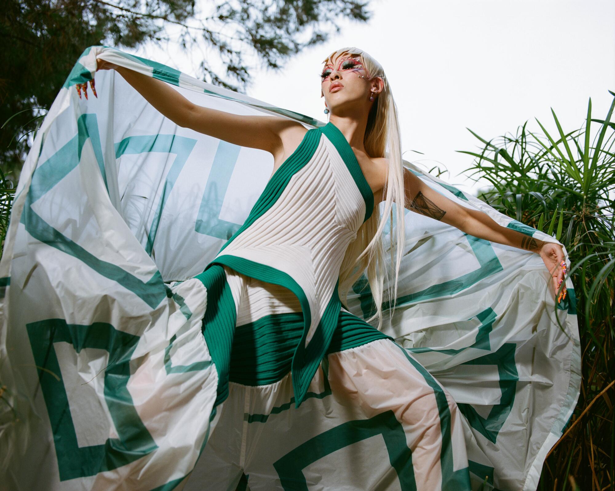 A model wears a one-shouldered tank over a skirt with a shawl, all in white fabric with green trim