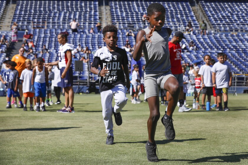 Hundreds of young San Diego football enthusiasts participated in annual free SDCCU Holiday Bowl Youth Football Clinic at SDCCU Stadium on Saturday. Drills and skills were led by Fast Play Athletics, including instruction by former NFL and other professional league players. Here, Darren Johnson (front) and Maurice Freeman warm up with high knees drills.