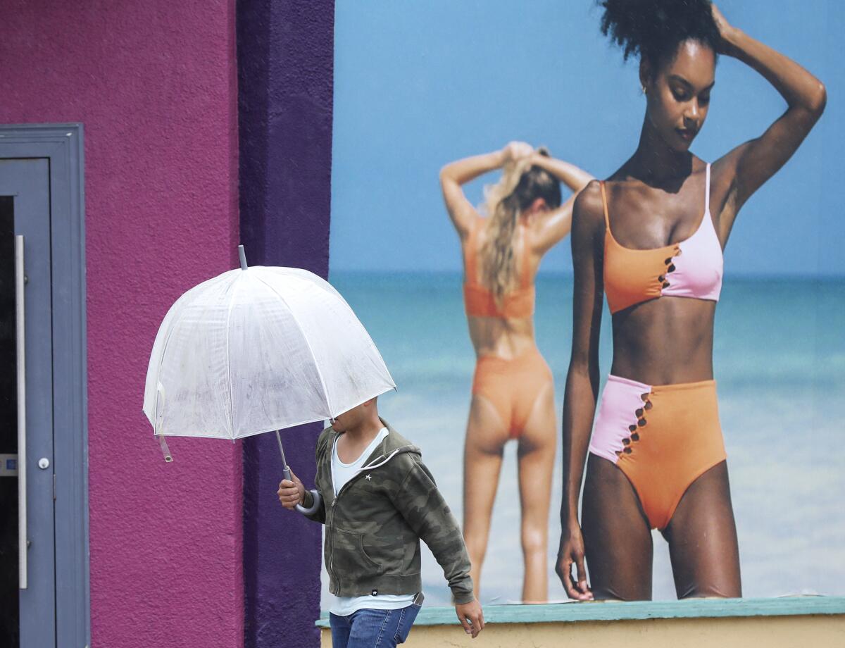 Wind and rain from Tropical Storm Hilary arrive in Mission Beach as a man walks by a bathing suit shop on Sunday.