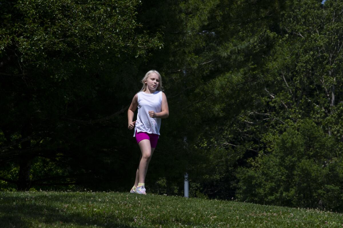 Becky Pepper-Jackson running across a green hill. Behihd her is more greenery. 
