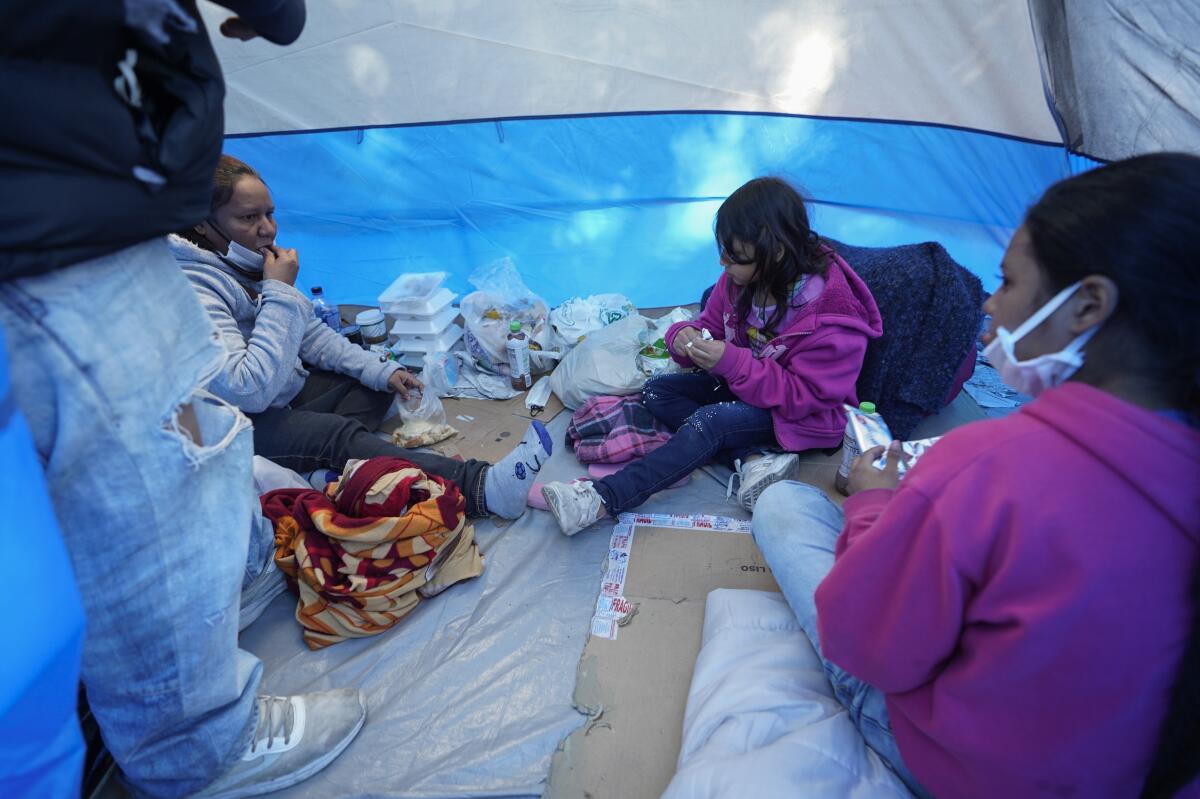 Three of four people in a tent share food while seated.
