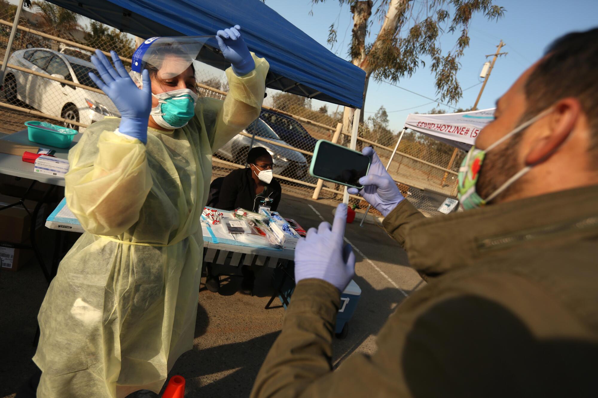 A man uses a phone to take video of a woman in full medical protective gear dancing