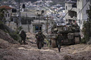 Israeli soldiers walk behind a tank in the Jenin camp