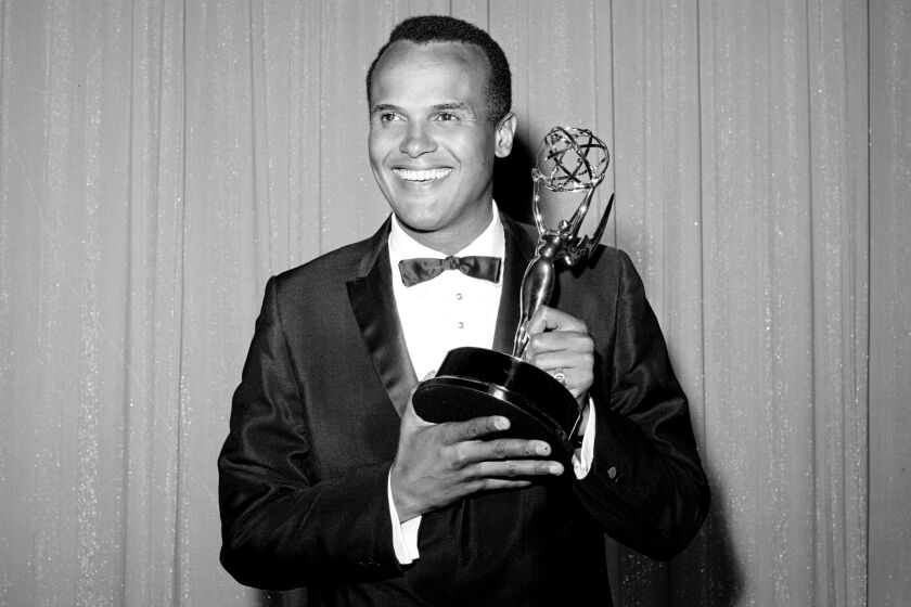 A black-and-white image of Harry Belafonte smiling, wearing a suit and holding an Emmy Award