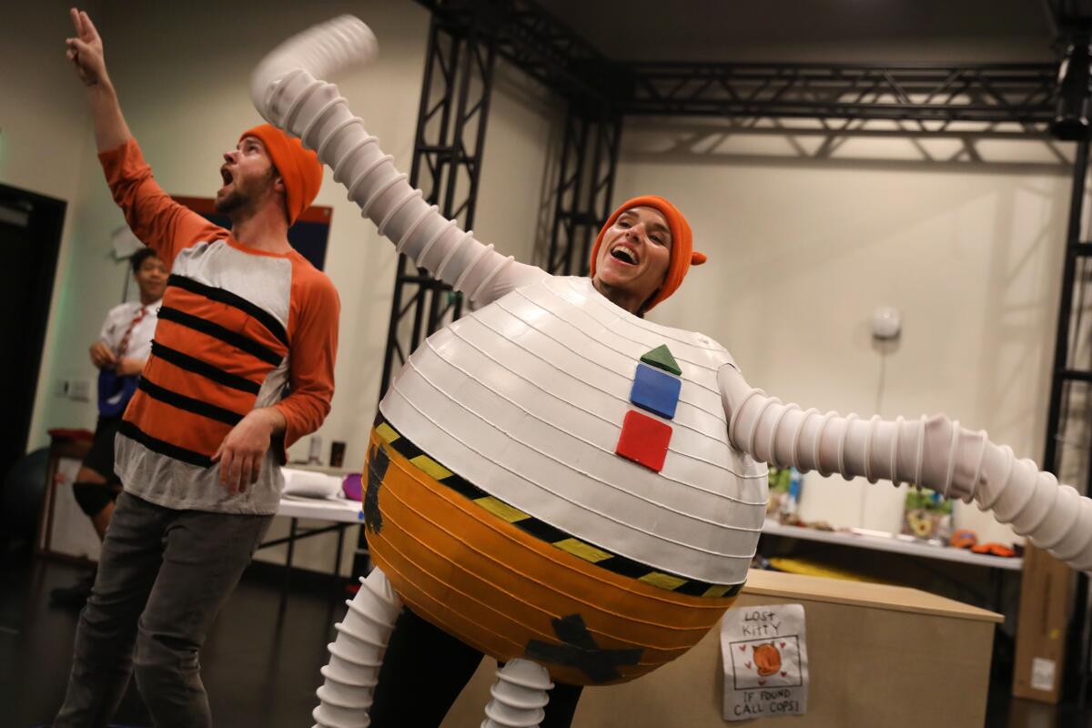 A man in orange and black stripes and a woman in a costume that looks like a ball with long ribbed arms and legs. 