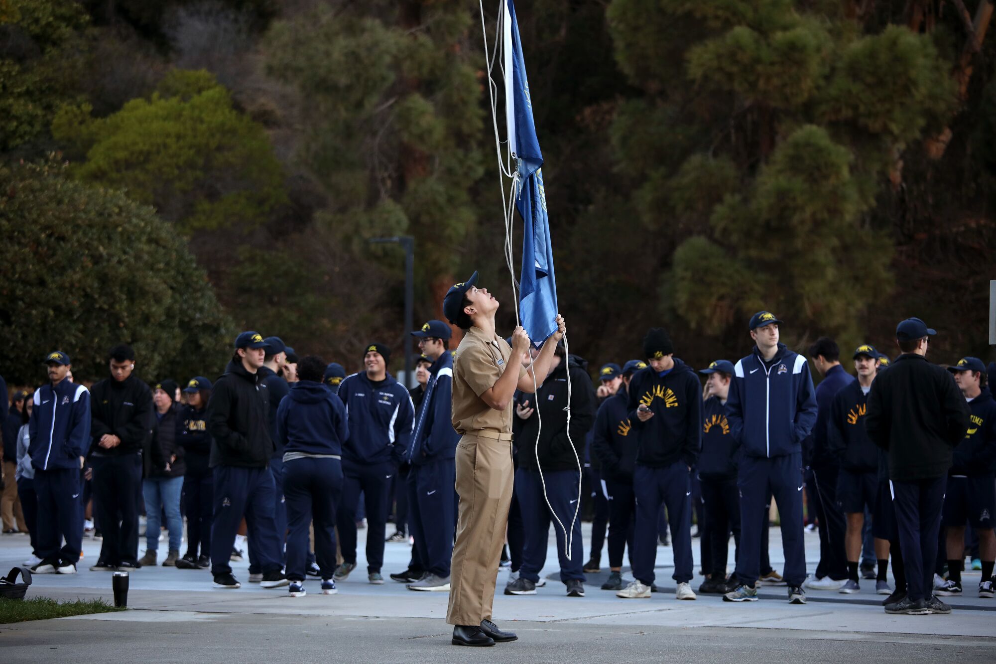 A person raises a blue flag outdoors as many people stand in the background.