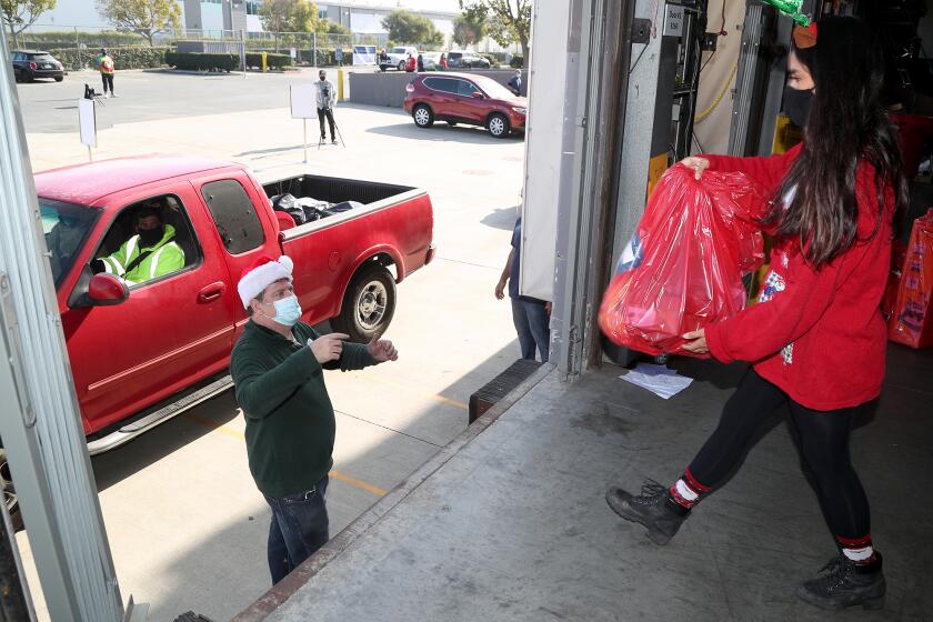 The Priority Center employees Arlette Carrion, right, brings a bag of holiday gifts items to Mike Littler, left, to give to a family during a drive-through event on Saturday in Huntington Beach.