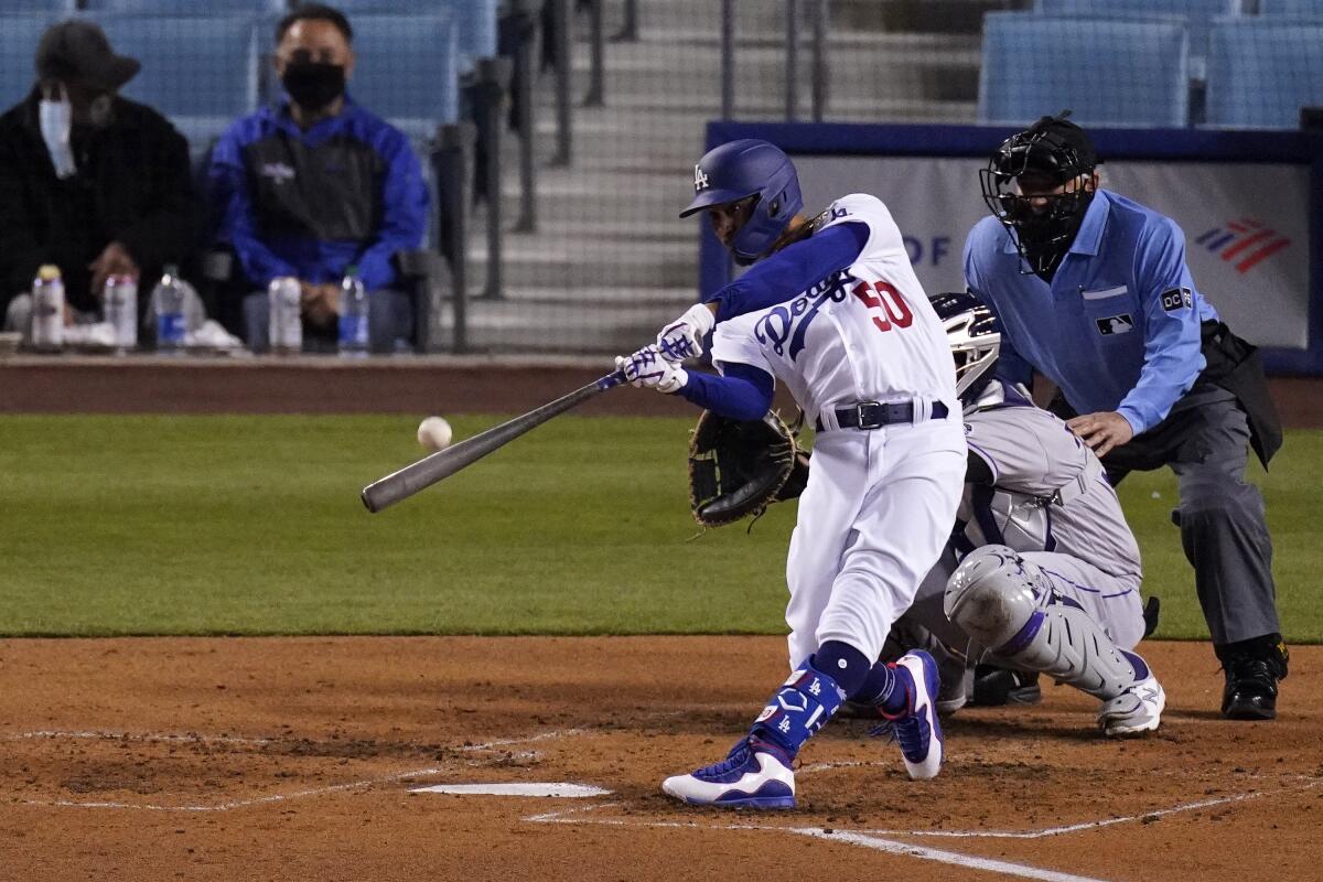 Los Angeles Dodgers' Mookie Betts, left, hits a solo home run as Colorado Rockies catcher Elias Diaz, center, watches along with home plate umpire Tom Hallion during the third inning of a baseball game Tuesday, April 13, 2021, in Los Angeles. (AP Photo/Mark J. Terrill)