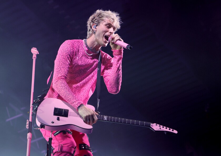 A singer in a pink shirt and pants holds a pink guitar and sings into a pink microphone.