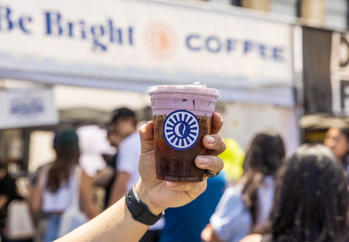 A hand holds out a plastic cup of cold brew that's topped with purple ube cream at Smorgasburg.