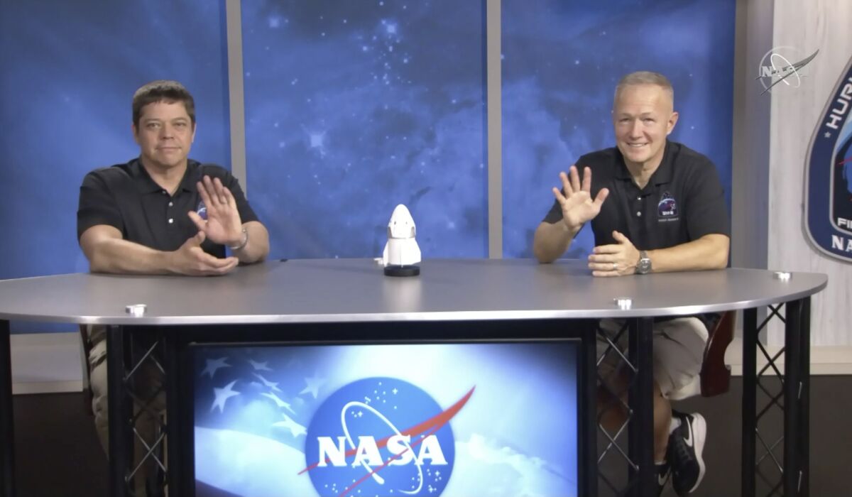 In this frame grab from NASA TV video, astronauts Bob Behnken, left, and Doug Hurley wave during a news conference, Tuesday, Aug. 4, 2020, in Houston. The two NASA astronauts returned to Earth on Sunday in a dramatic, retro-style splashdown carried out by Elon Musk's SpaceX company. (NASA TV via AP)