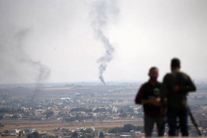 TV journalists work on a hilltop in Ceylanpinar, Sanliurfa province, southeastern Turkey, as in the background smoke billows from a fire in Ras al-Ayn, Syria, Sunday, Oct. 20, 2019. Turkey's defense ministry says one soldier has been killed amid sporadic clashes with Kurdish fighters in northern Syria, despite a U.S.-brokered cease-fire. The ministry also said it allowed a 39-vehicle humanitarian convoy to enter Ras al-Ayn, a key border town that's seen some of the heaviest fighting. (AP Photo/Lefteris Pitarakis)