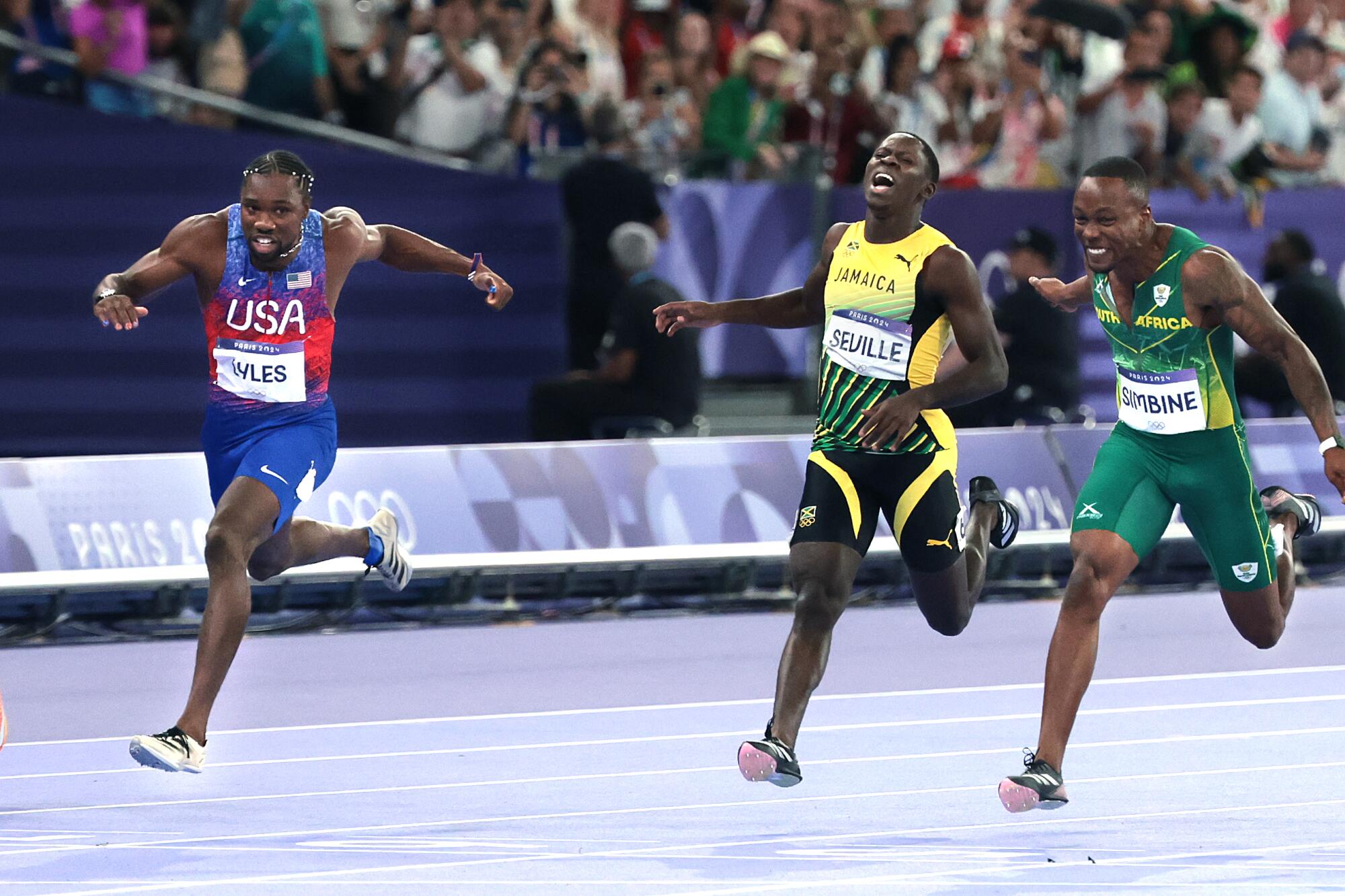 American Noah Lyles, left, crosses the finish line to win gold in the men's 100 meters at the Paris Olympics on Sunday.