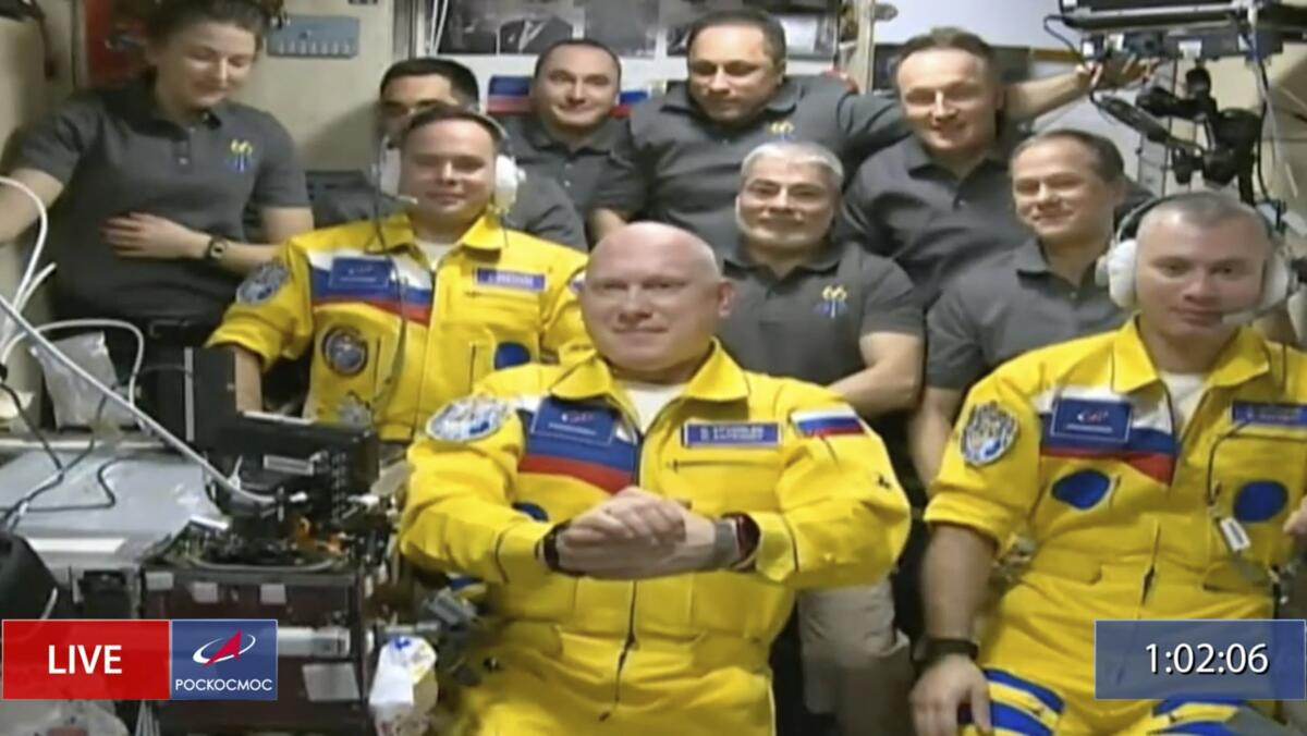 Space station inhabitants pose as a group, with three latest arrivals in blue-and-yellow suits in front