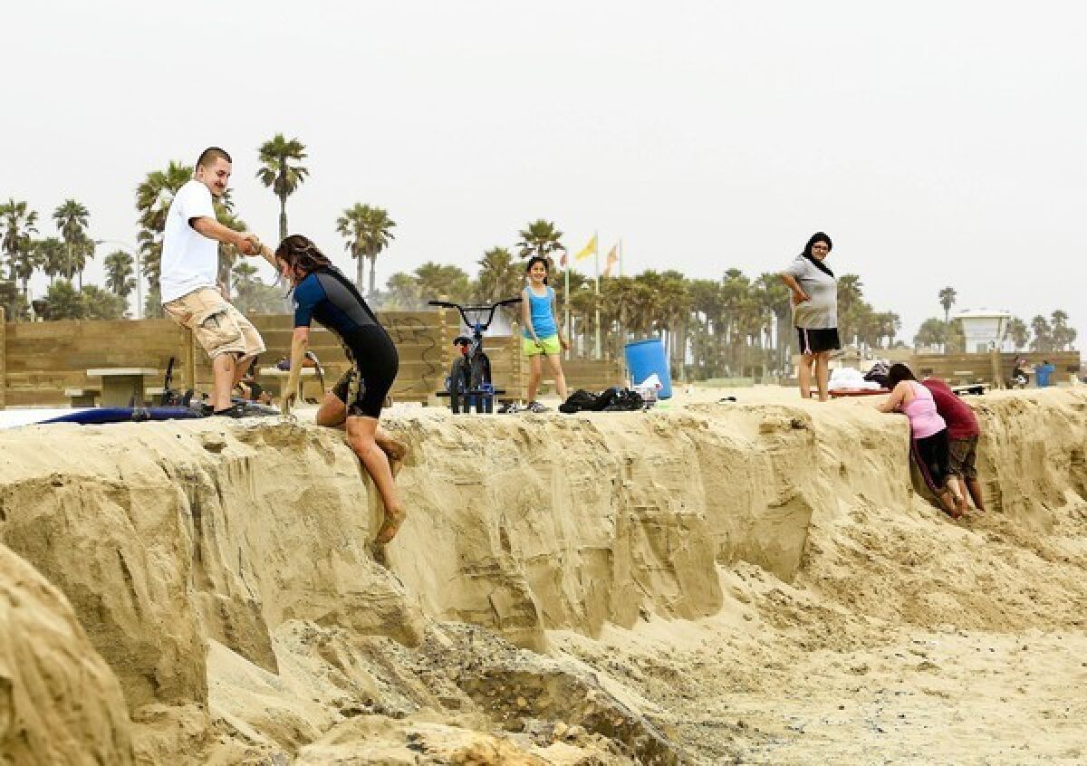 David Guerrero of Oxnard lends a hand to Eden Espinoza of Port Hueneme at a wall caused by sand erosion on Port Hueneme beach.