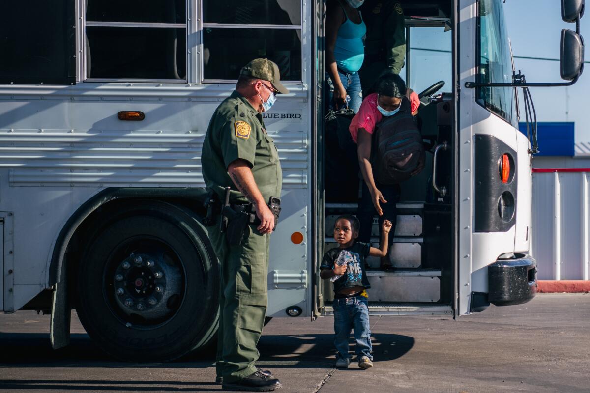 A child and a woman exit a bus. A uniformed officer waits at the bus door.