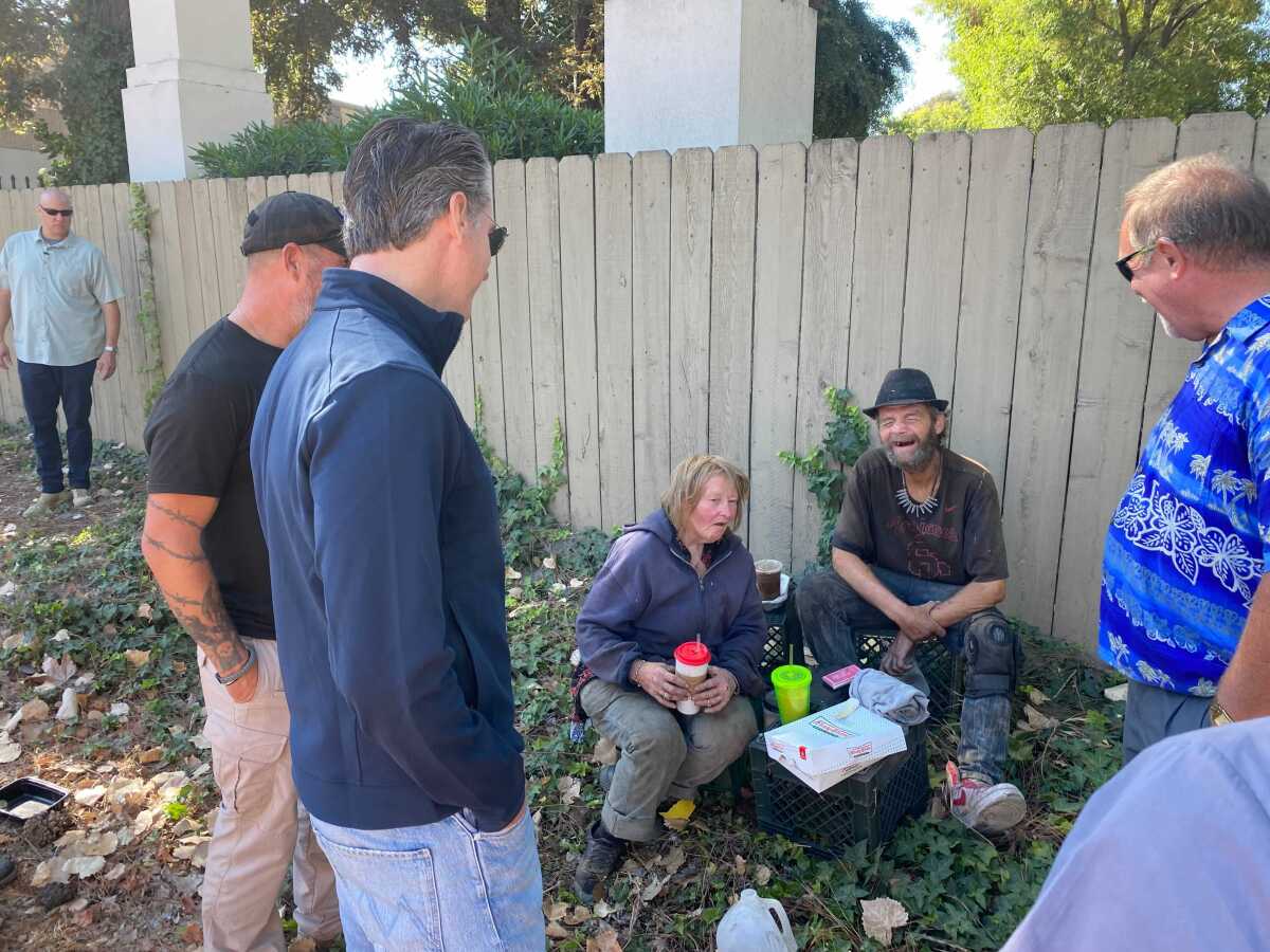 Gov. Gavin Newsom speaks to a homeless couple sitting on egg crates on the ground