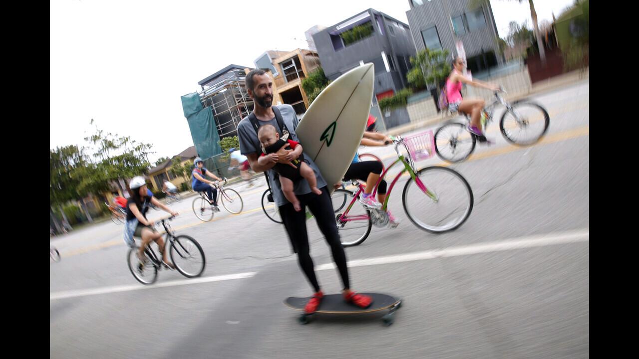 David Aguilar of Mar Vista skateboards while carrying his surfboard and nephew Alonso Metcalf, 2 months, along Venice Boulevard in Venice. Culver City and Venice is host to the latest edition of the CicLAvia bike festival on Sunday.