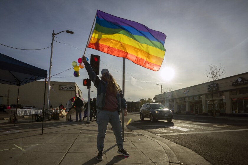 A person in silhouette waves a rainbow flag