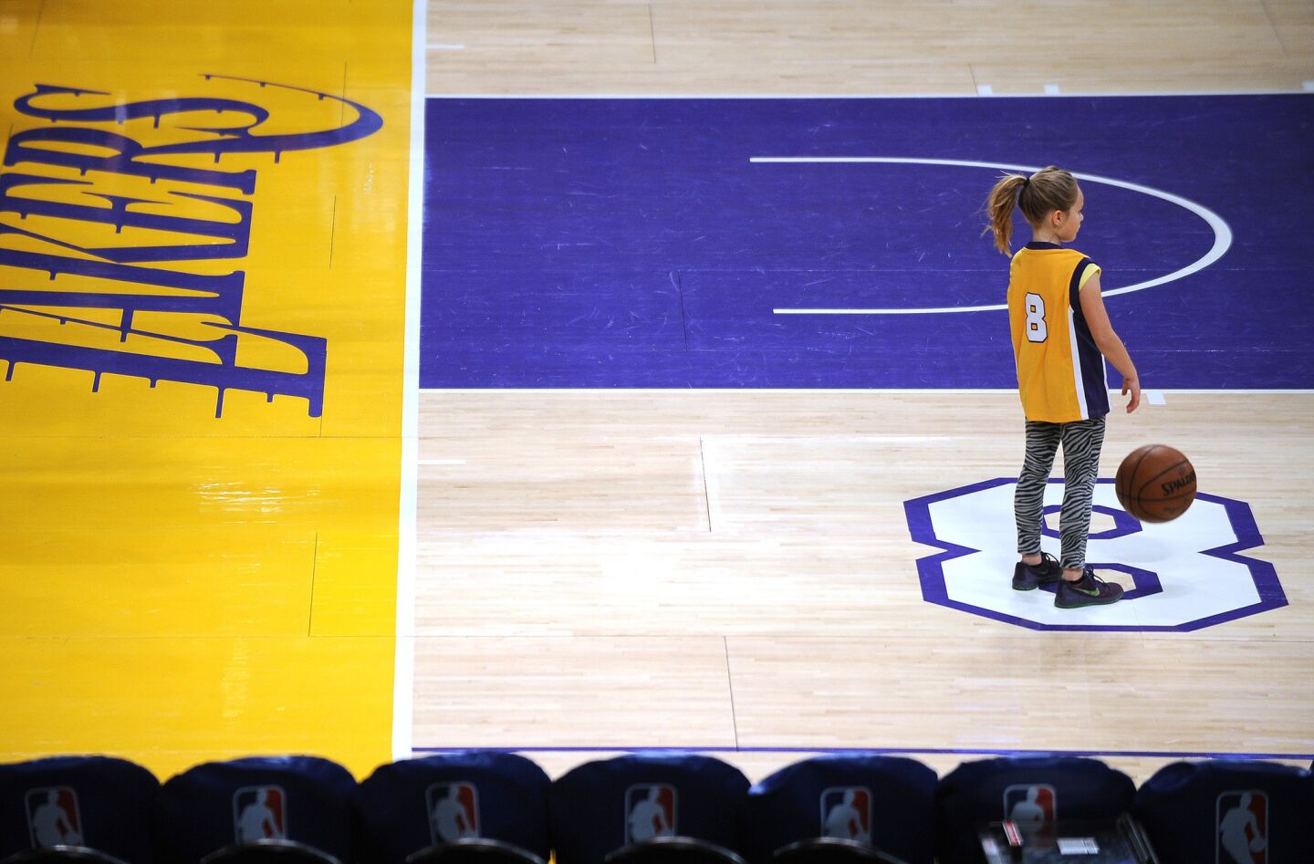 A young girl, sporting Kobe Bryant's original No. 8 Lakers jersey, bounces a ball on the court before the future Hall-of-Famer's final game.