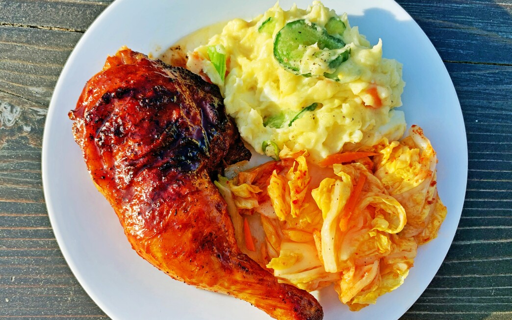 Gochujang-glazed grilled chicken on a white plate with potato salad and kimchi.