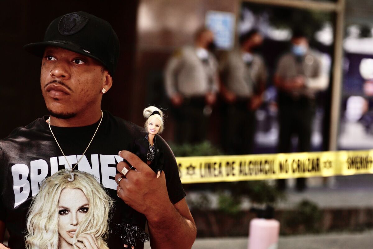 A person wears a "Britney" T-shirt and holds a doll.