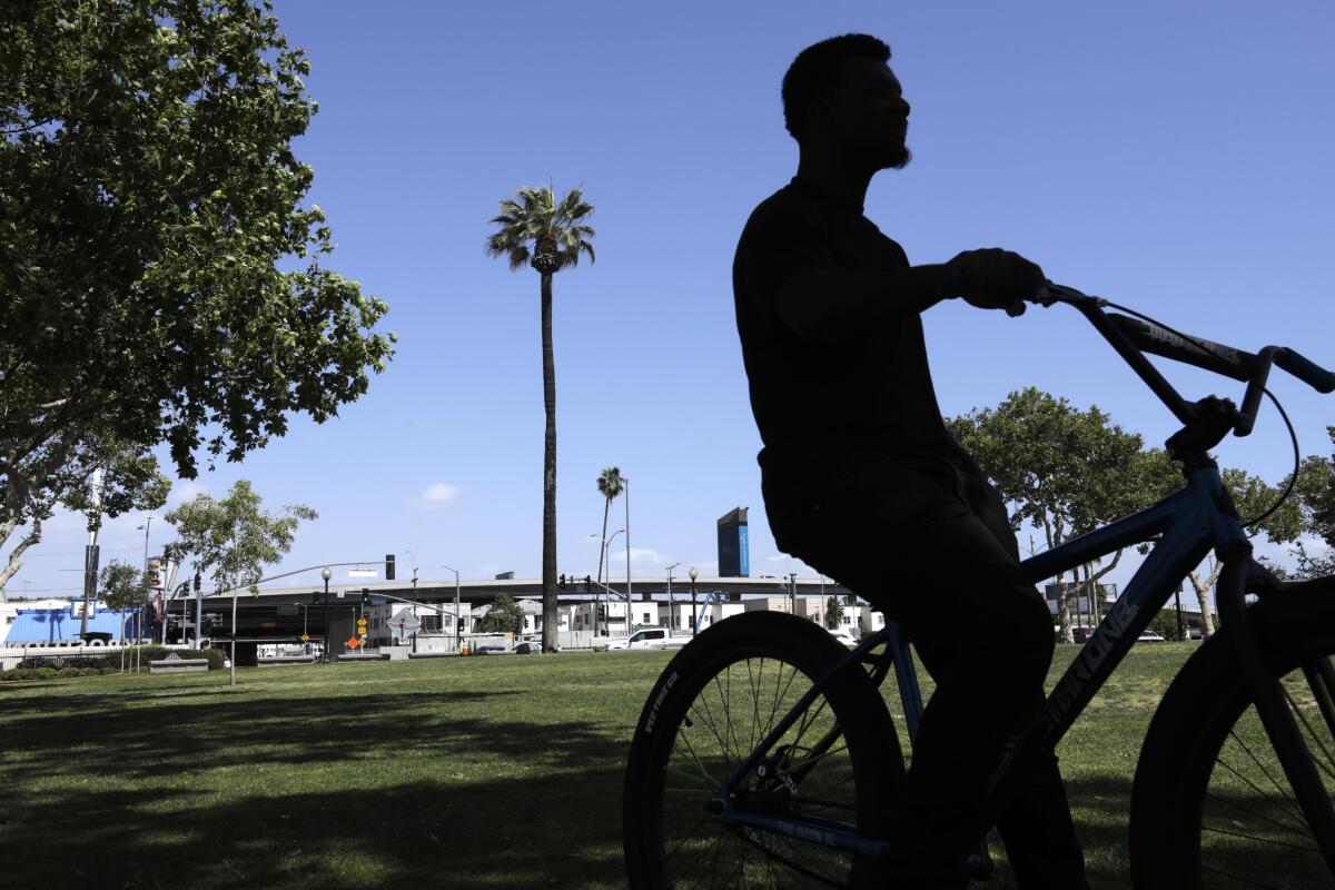 Abraham Augustine sits on his bike near what may be one of Los Angeles's oldest palm trees