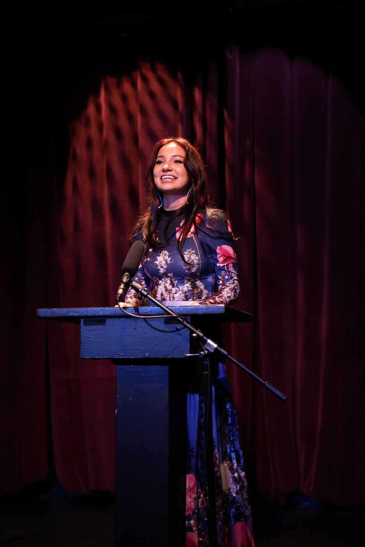 A woman stands at a podium in the spotlight.