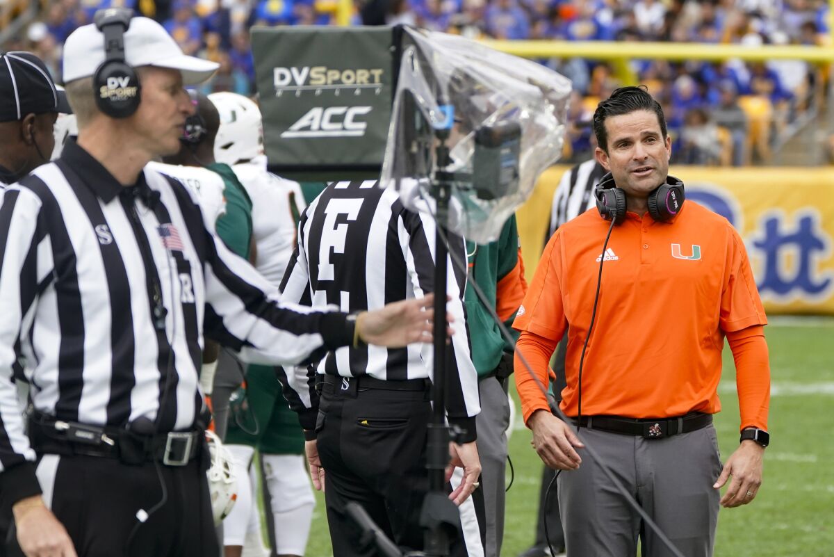 Miami head coach Manny Diaz, right, watches as referee Jeff Heaser, left, looks at a review screen after a targeting penalty was called against Miami during the first half of an NCAA college football game, Saturday, Oct. 30, 2021, in Pittsburgh. The review determined no targeting. (AP Photo/Keith Srakocic)