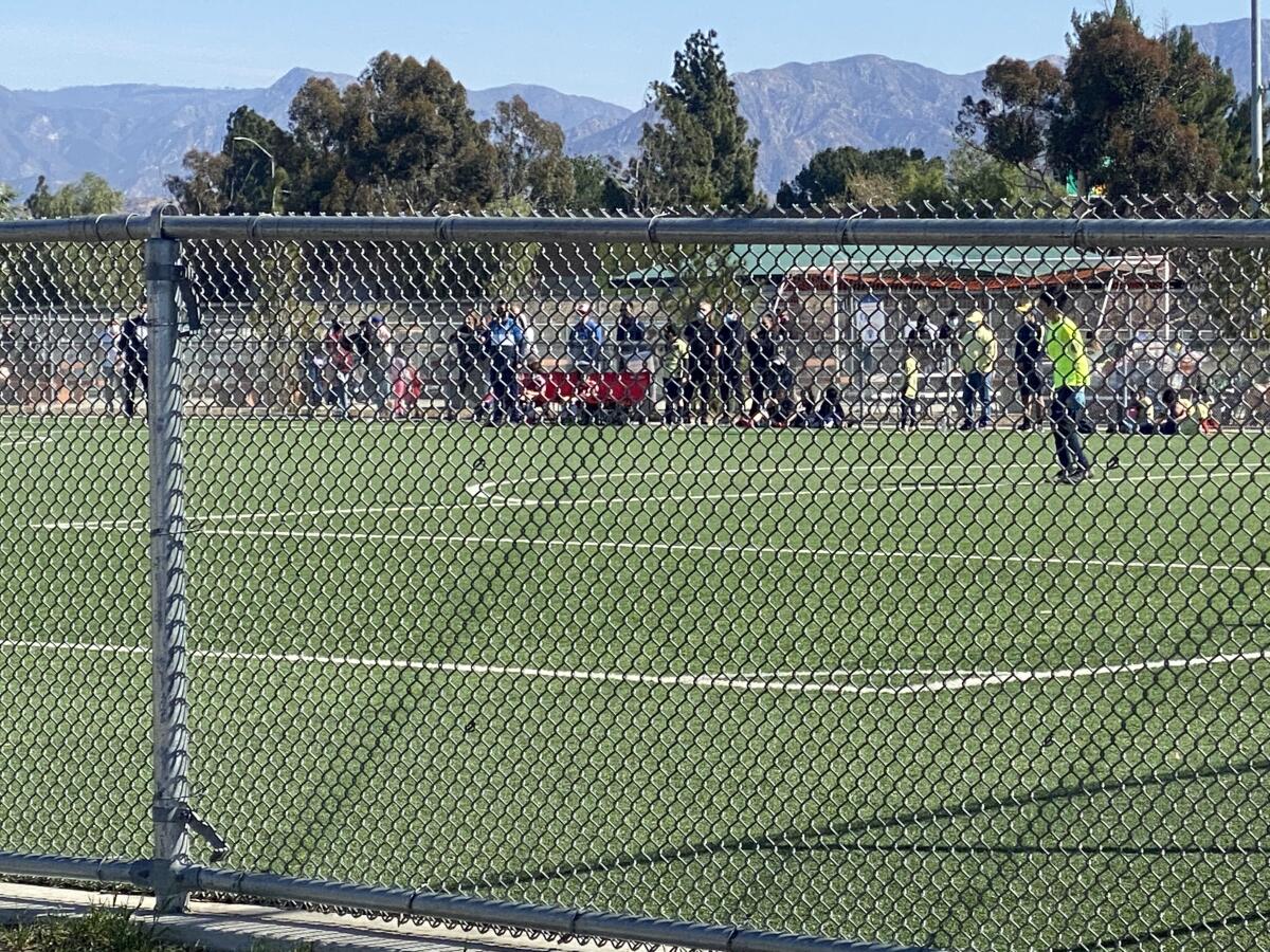 A youth soccer game on a field as seen through a chain link fence.