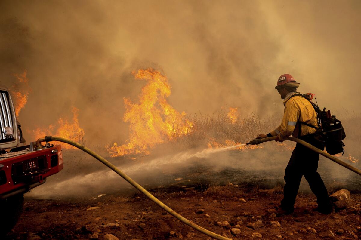 A firefighter sprays water while trying to keep the Electra Fire from spreading in the Pine Acres community of Amador County, Calif., on Tuesday, July 5, 2022. (AP Photo/Noah Berger)
