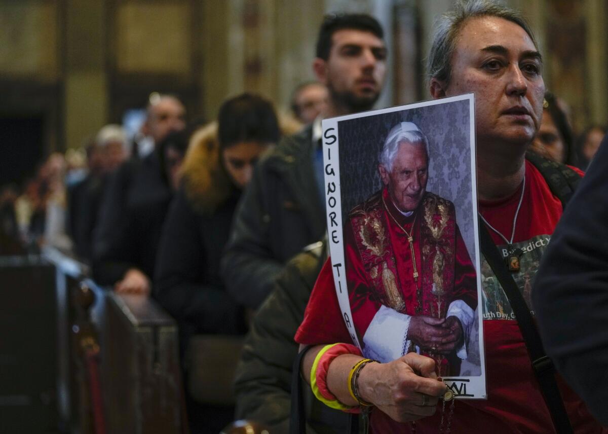 A person in line to view the pope's body holds a picture 