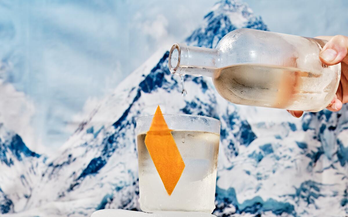 A drink is poured into a glass with a snow-covered mountain in the background