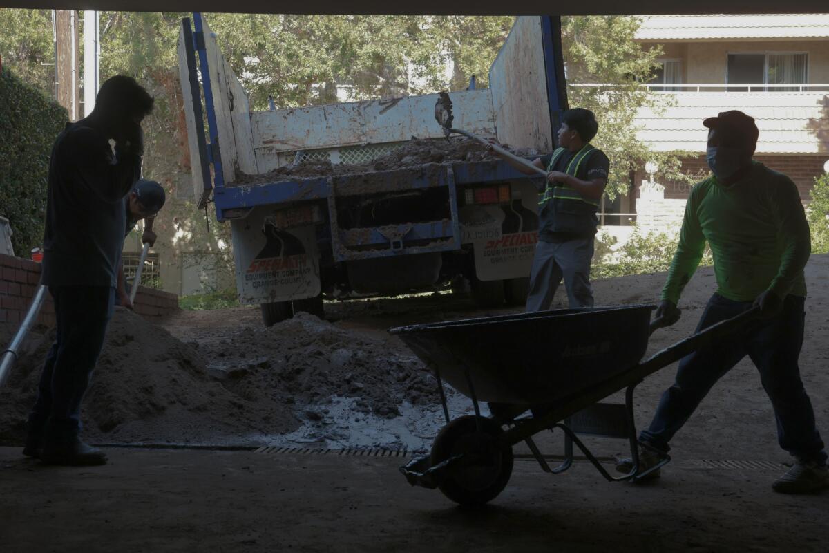 Workers shovel mud from a driveway at an apartment complex on Palm Avenue that was damaged by a water main rupture.