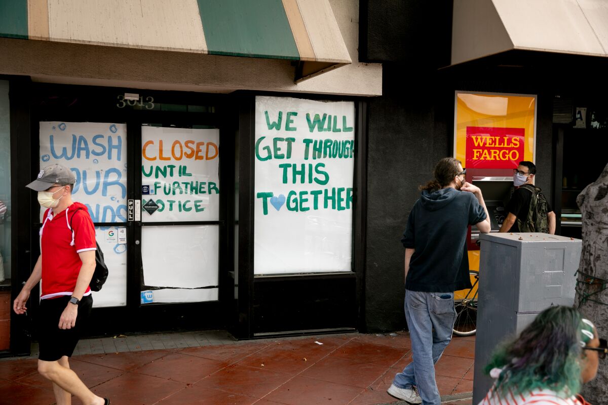 People walk by a business papered with signs reading "Closed Until Further Notice" and "Wash Your Hands."