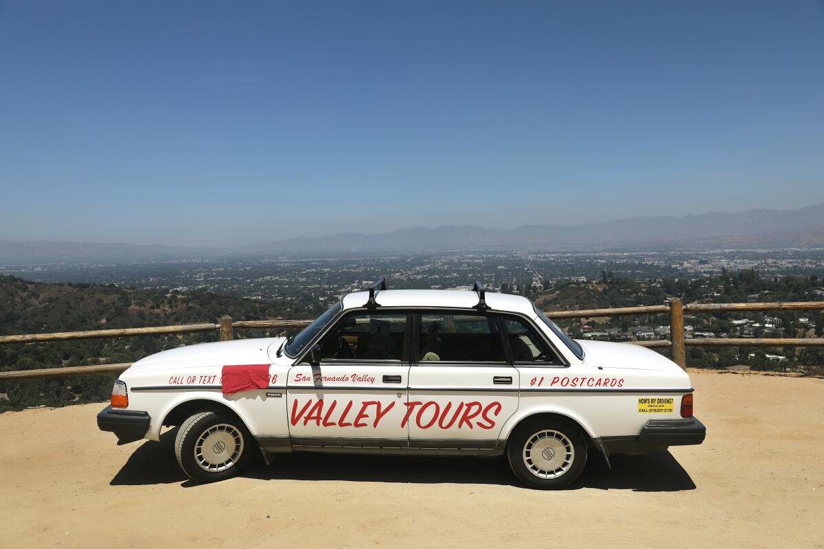 A white Volvo parked before a fence with a grand view of the Valley.