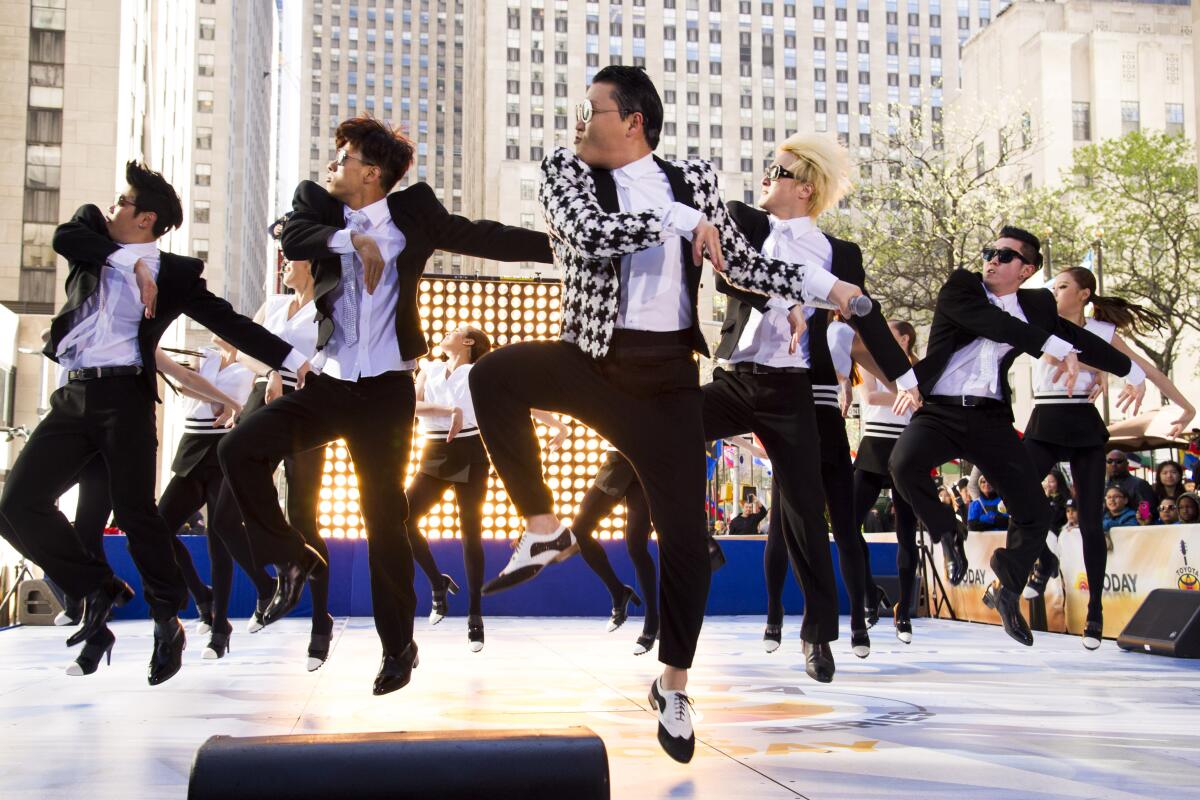 A troupe of singers and dancers, one wearing a checked jacket, jumps into the air