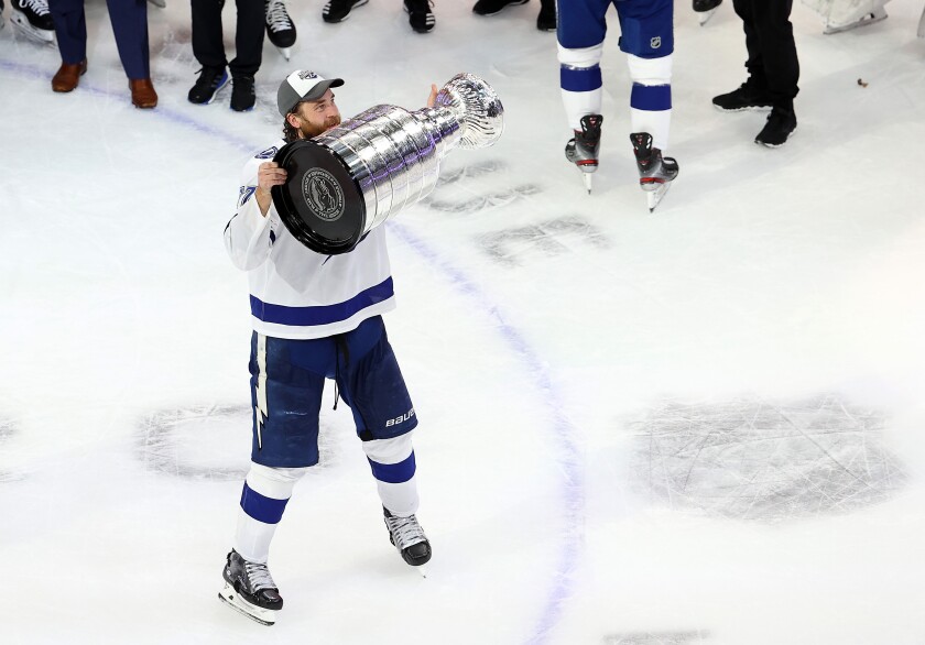 A hockey player, on the rink, holds up the Stanley Cup.