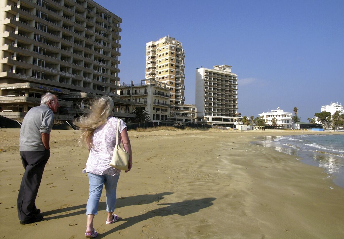 FILE - Friday, Jan.17, 2014 file photo, a couple walk on the beach by the deserted hotels in an area used by the Turkish military in the Turkish occupied area in abandoned coastal city of Varosha, in Famagusta, in southeast of island of Cyprus. Cyprus government spokesman Kyriakos Koushos says on Tuesday, Oct. 6, 2020, formal protests will be lodged at the United Nations, the European Union and other international organizations over Turkey's decision to open up to the public a stretch of beach in fenced-off Varosha. Koushos said the move contravenes international law and U.N. Security Council resolutions on Varosha that has remained uninhabited for 46 years. (AP Photo/Petros Karadjias, File)